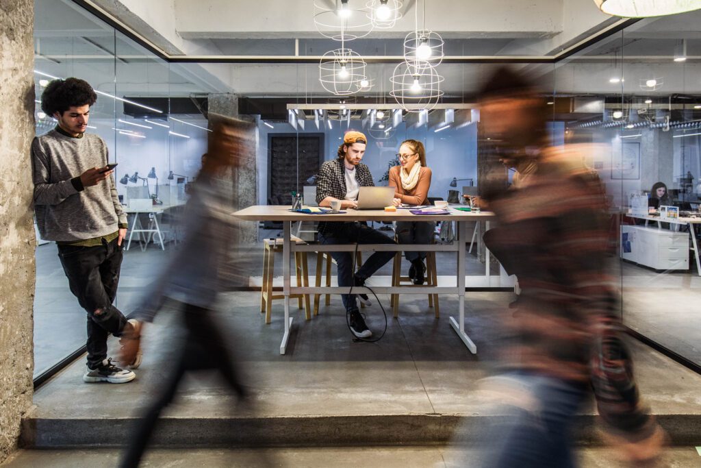 Group of young freelancers working on wireless technology at casual office. Some people are in blurred motion.