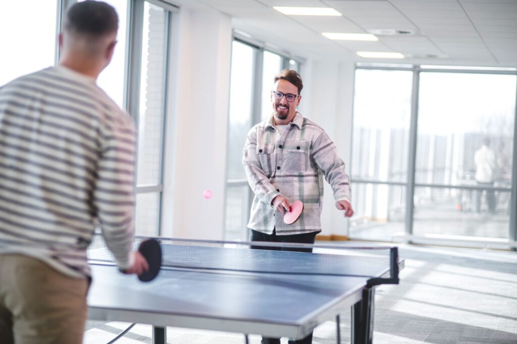 Two co-workers smiling and playing ping pong