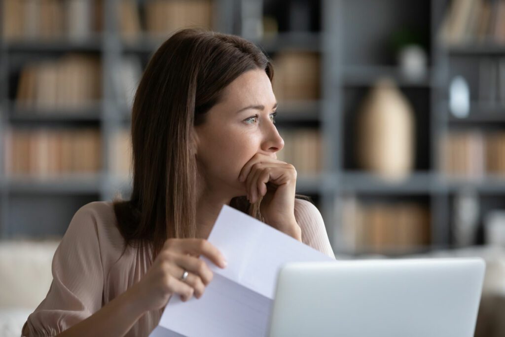 Head shot stressed young woman holding paper document, bank debt notification, thinking of financial troubles, looking away.