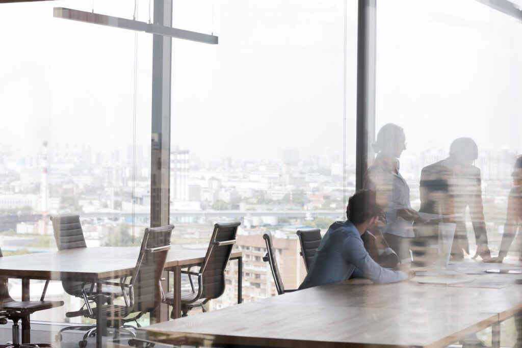 Business team meeting in contemporary business center, talking at office conference table, negotiating on project in modern interior with big panoramic window.