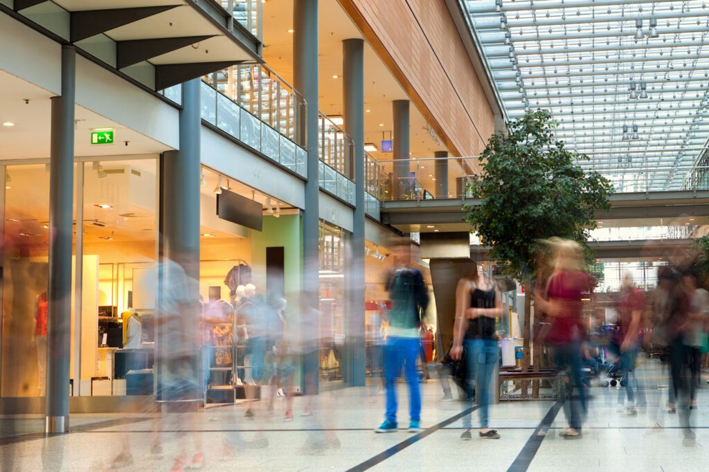 Shopping mall at rush hour, with many unrecognizable blurred people buying sales goods in various boutiques and shops.