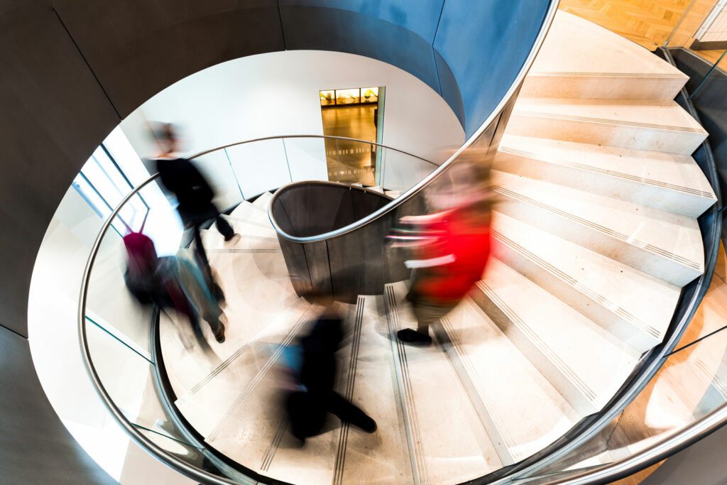Blurred Motion of Urban People Running down Futuristic Modern Spiral Staircase