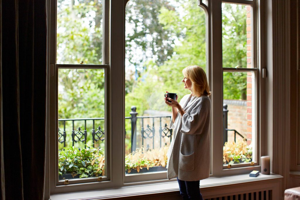 Shot of a mature woman drinking tea while looking out of her living room window