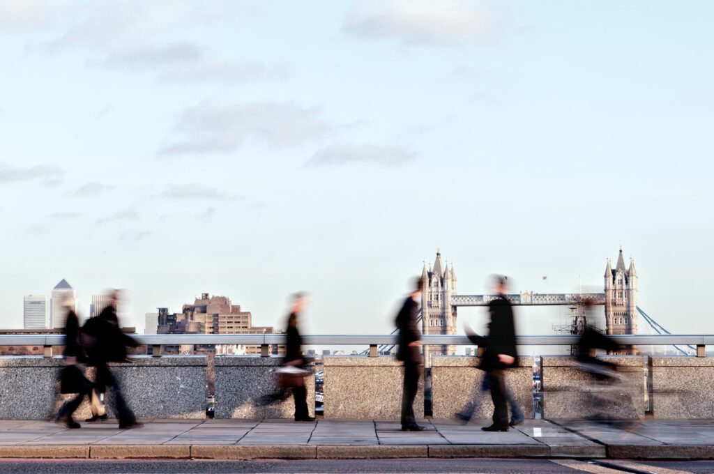 Blurred commuters walking along London Bridge with landmarks in the background