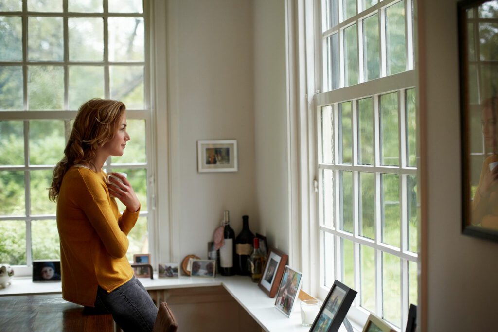 Side view of thoughtful woman looking through window while having coffee in cottage