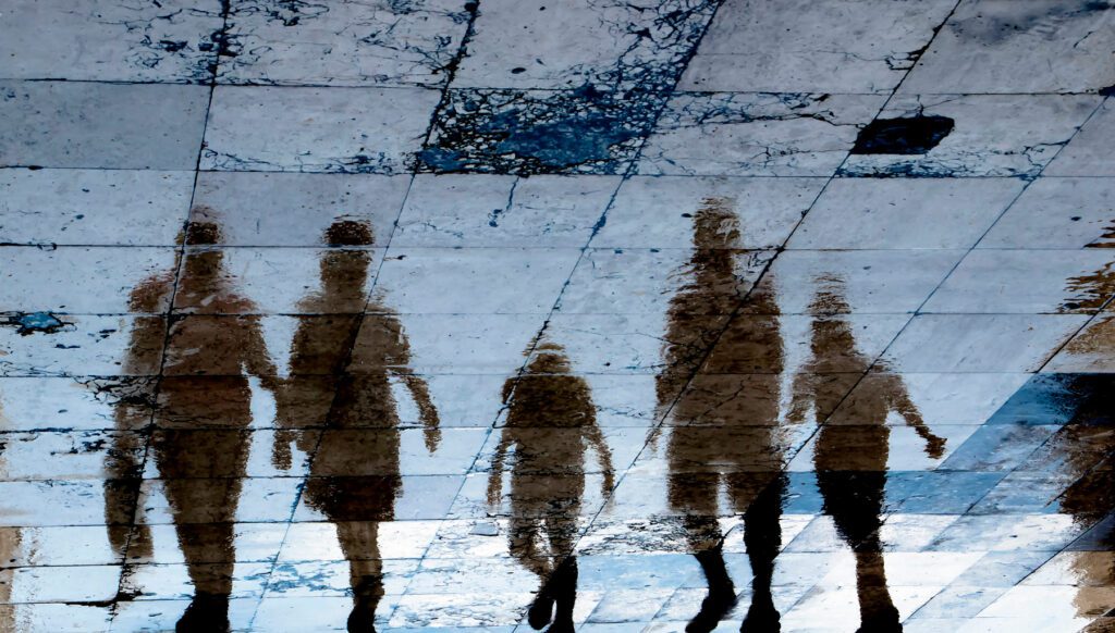 Blurry reflection shadow silhouette on wet city sidewalk of mysterious people walking away the night