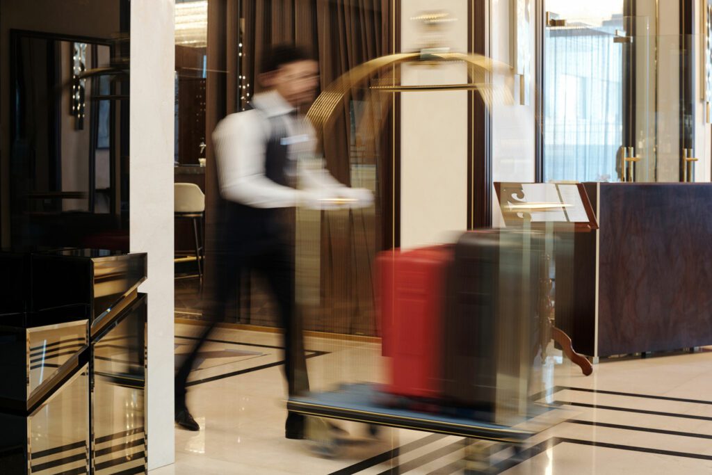 Blurry motion of bellboy walking fast along lounge or hall of luxurious five star hotel and pushing cart with baggage of tourists