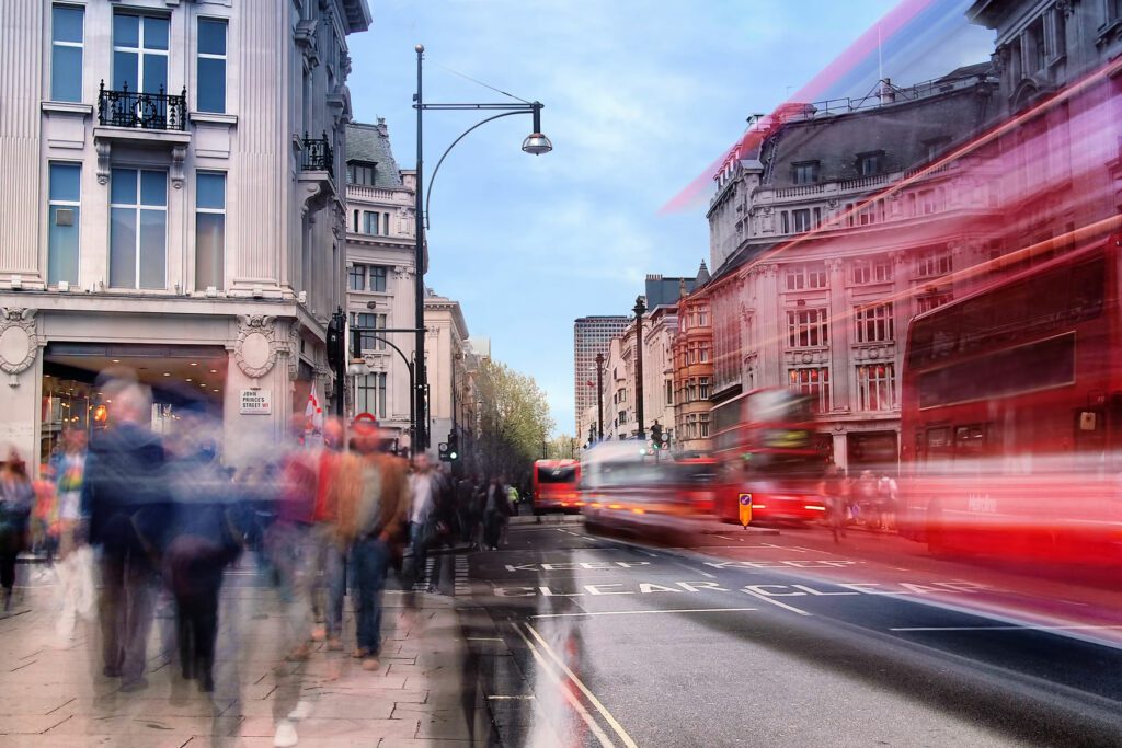 Daytime long exposure on Oxford Street near Oxford Circus on a busy weekend afternoon as shoppers walk past and several buses drive by