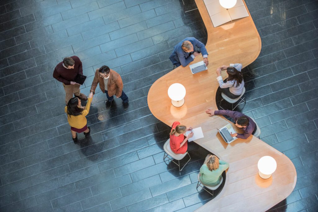 Group of businessmen and women seen from above, sitting at modern shaped desk.