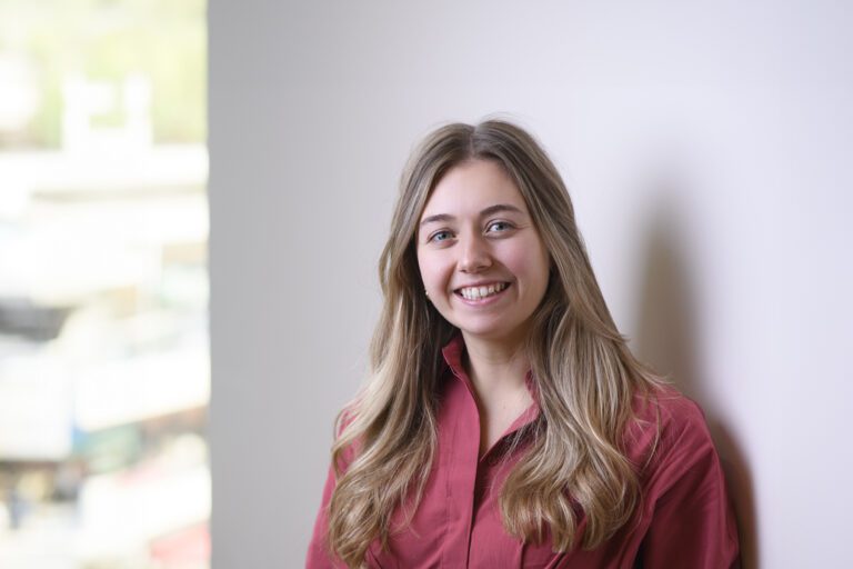 Charlotte Pottow is a smiling young woman with long blonde hair wearing a red collared shirt.