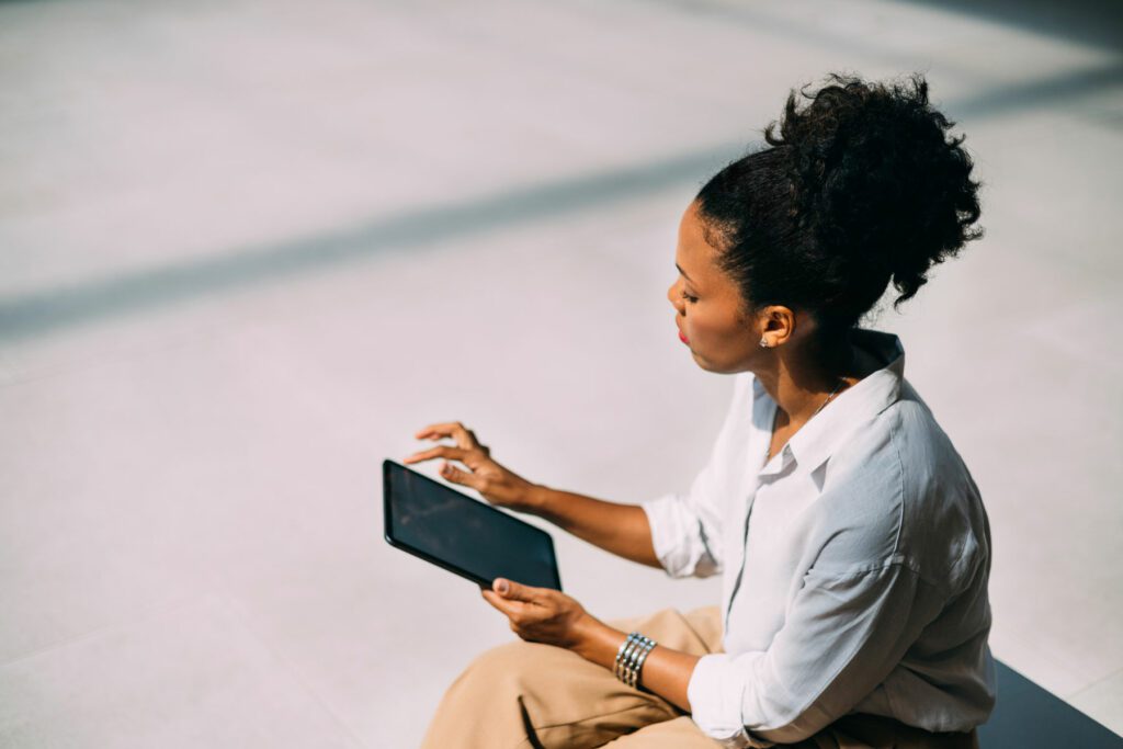 Women scrolling on her tablet while sitting on a street bench.
