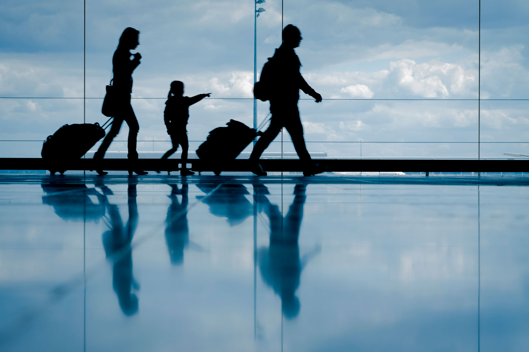ihouette of young family with luggage walking at airport, girl pointing at the window
