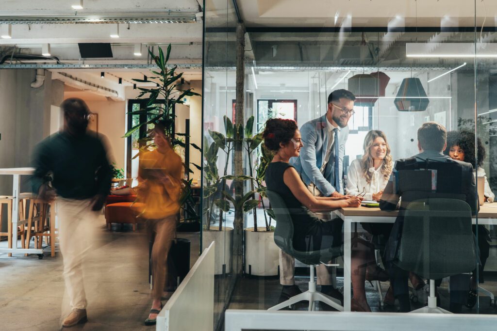 A diverse team of professionals engaged in a collaborative business meeting inside a modern glass-walled conference room