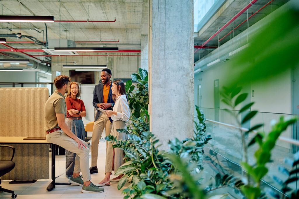 Group of diverse businesspeople engaged in a project discussion within a modern office filled with lush plants, fostering collaboration and creativity