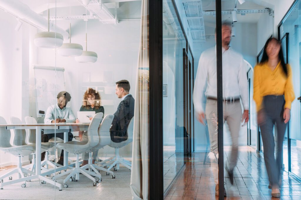 Business persons having a business meeting inside of an office board room while their colleagues are walking in blurred motion