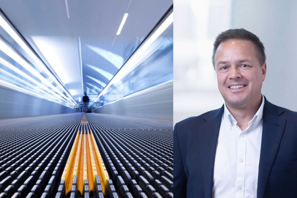 A blurred moving travelator on the left, viewed from a low angle, with a smiling man in a suit standing against a light background on the right.