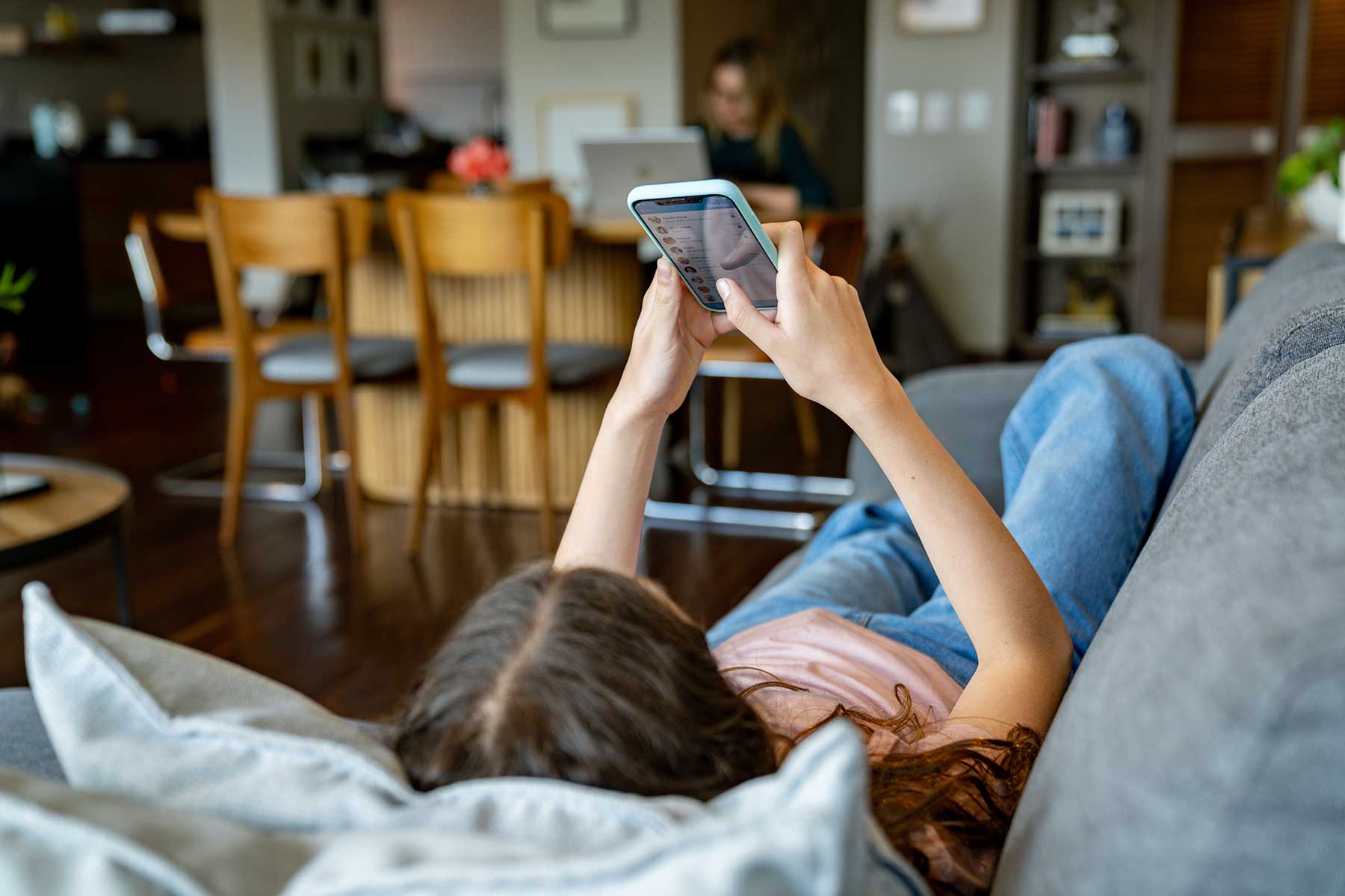 Teenage girl at home looking at social media on her cell phone while lying on the couch