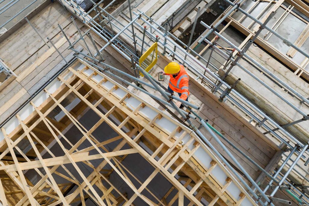 Construction worker on building site showing housebuilding,roof trusses, scaffolding and completed house