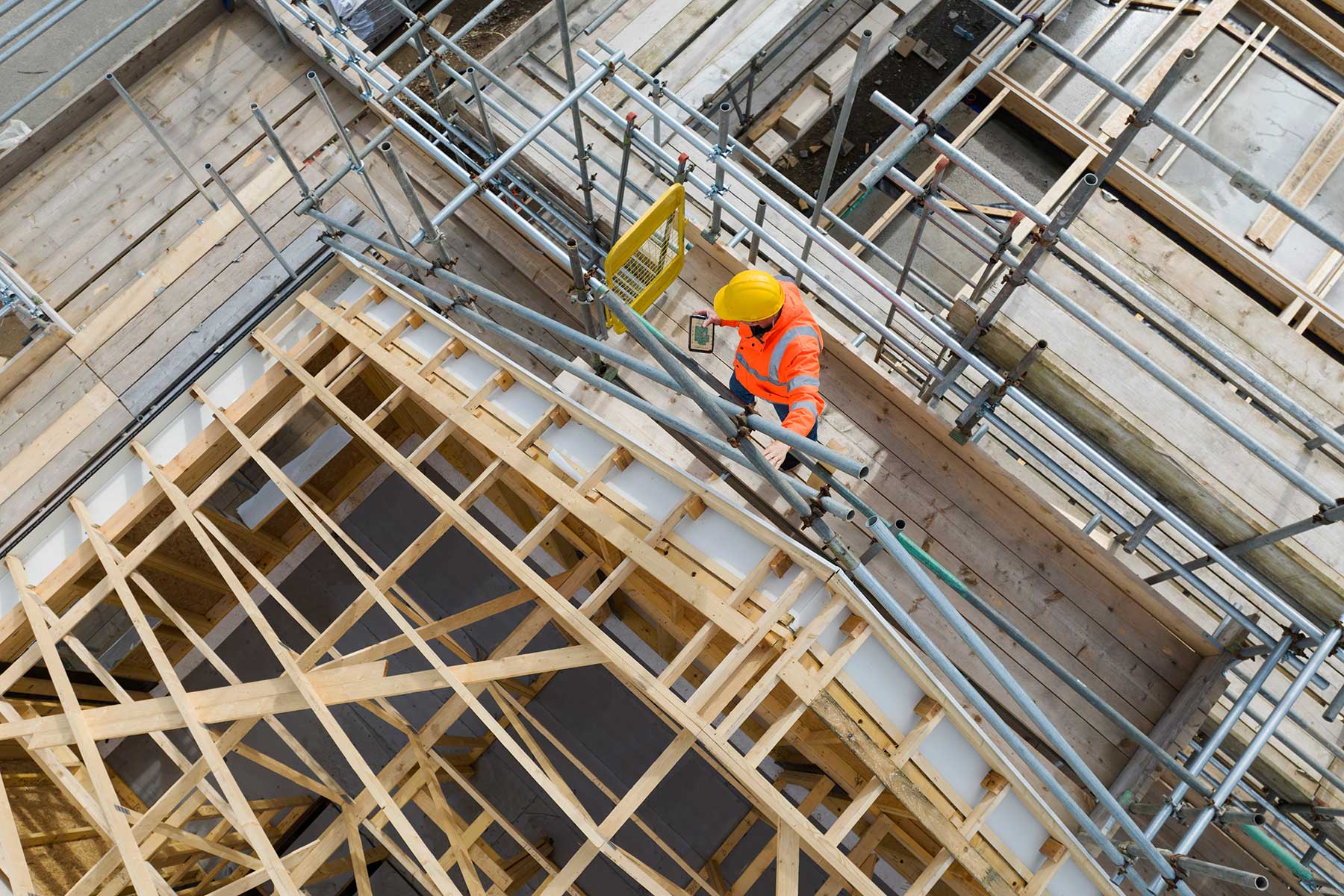 Construction worker on building site showing housebuilding,roof trusses, scaffolding and completed house