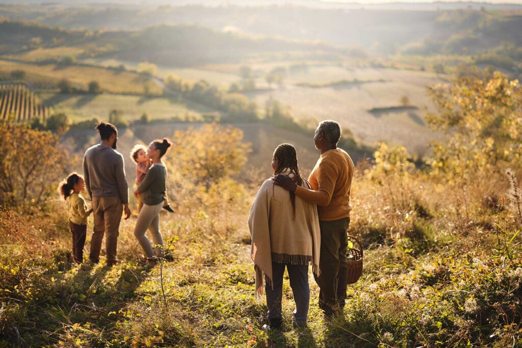 Back view of embraced grandparents looking at their family on a field in autumn day.