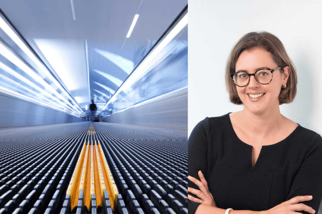 A woman with glasses and a black top smiles with arms crossed, next to a motion-blurred moving walkway in an indoor space.