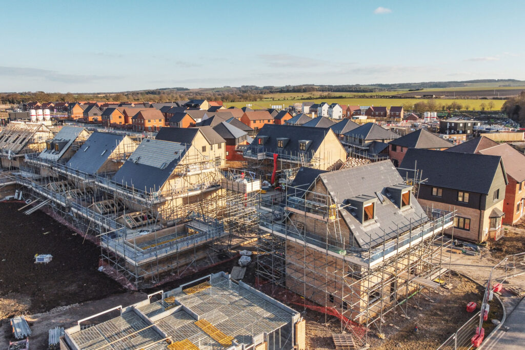 Aerial view of a residential construction site featuring multiple houses in various stages of completion surrounded by scaffolding.