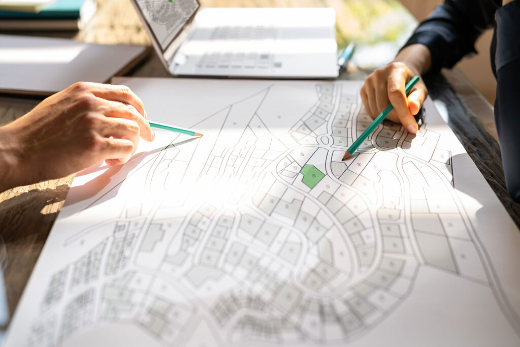 Two people use pencils to review a land development plan on a large paper map spread across a desk.