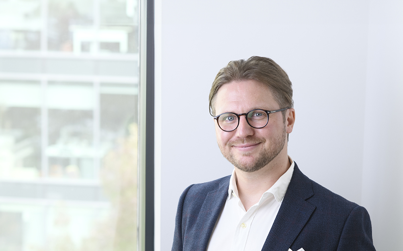 Joshua Bryant is a smiling man with light brown hair and glasses, wearing a white shirt and dark blazer.